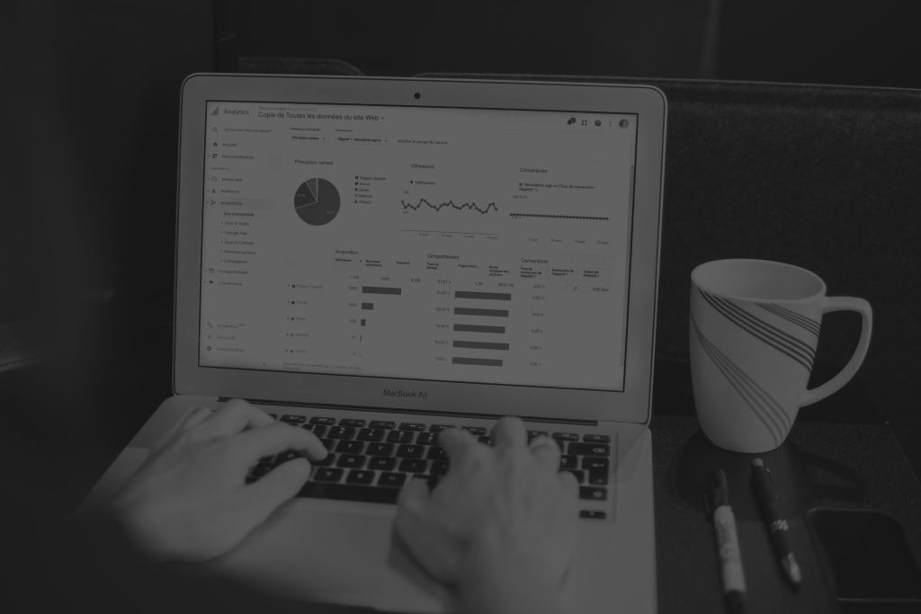 Laptop displaying data next to pens and a white mug