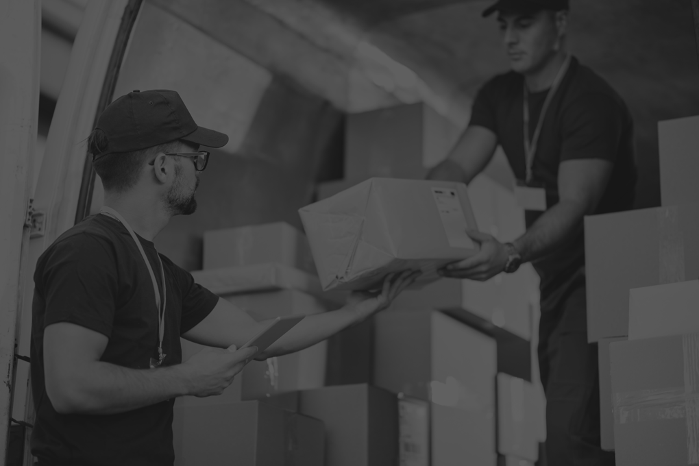 young-courier-using-touchpad-while-loading-packages-with-his-coworker-delivery-van