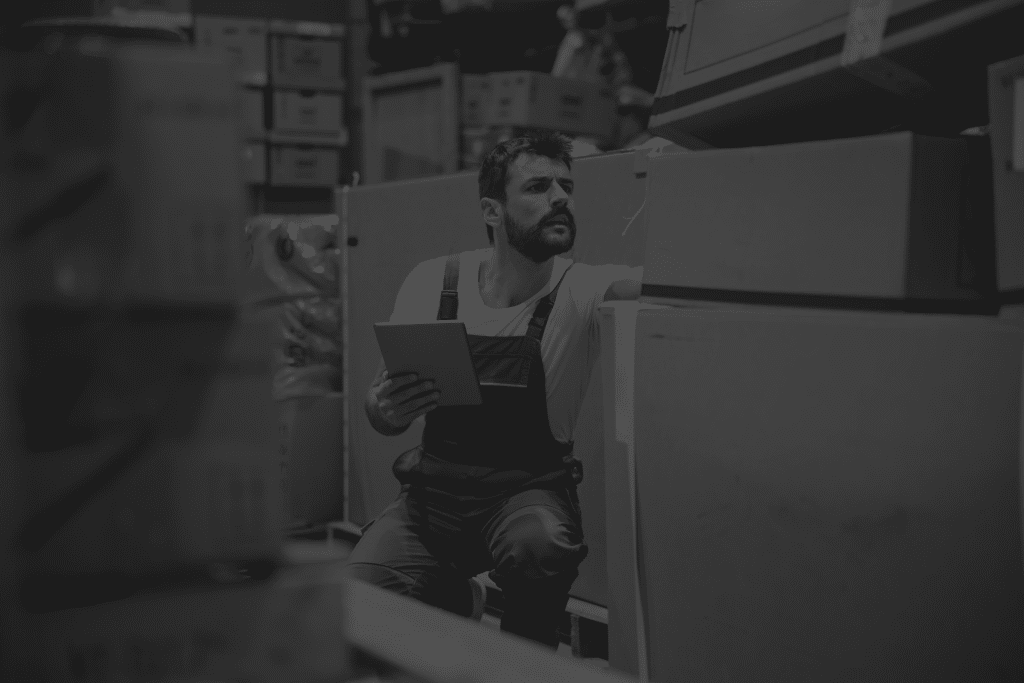 bearded-tattooed-hardworking-blue-collar-worker-overalls-crouching-storehouse-using-tablet-checking-inventory