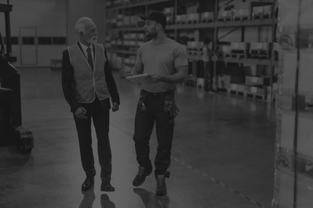 warehouse-worker-mature-businessman-talking-while-going-through-paperwork-industrial-building-ipaas-black-and-white