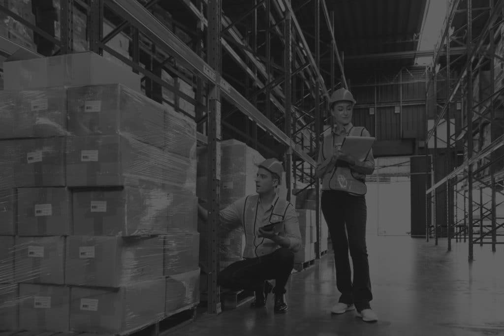 Warehouse workers with clipboards standing by racks and checking inventory in warehouse. Image in black and white.