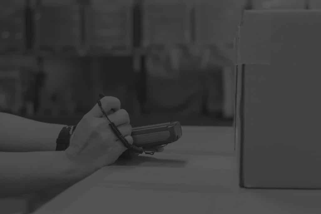 Closeup of man in warehouse writing on handheld with boxes around him. Image in black and white