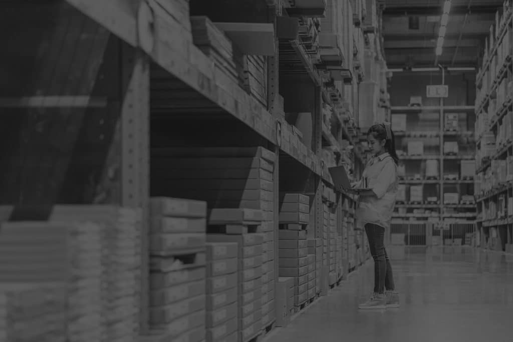 Black and white image of female warehouse worker on laptop checking inventory