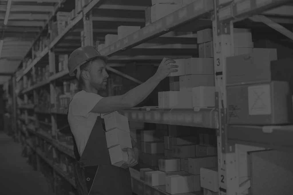 warehouse worker wearing hardhat picking boxes of racking black and white