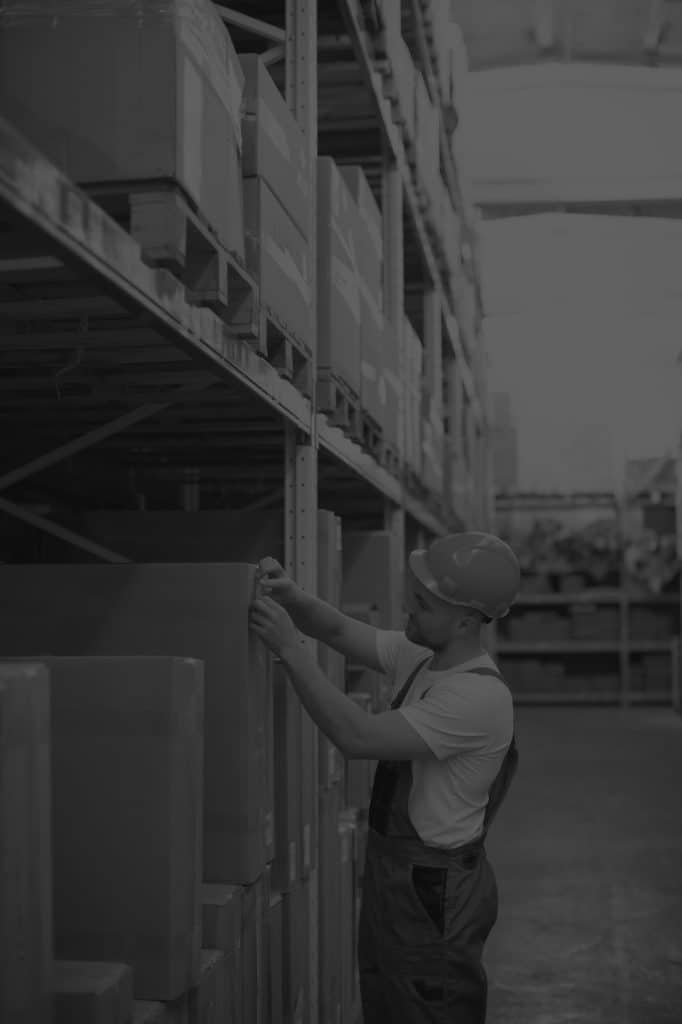 image of warehouse worker wearing hardhat pciking box off racking. Black and white image.