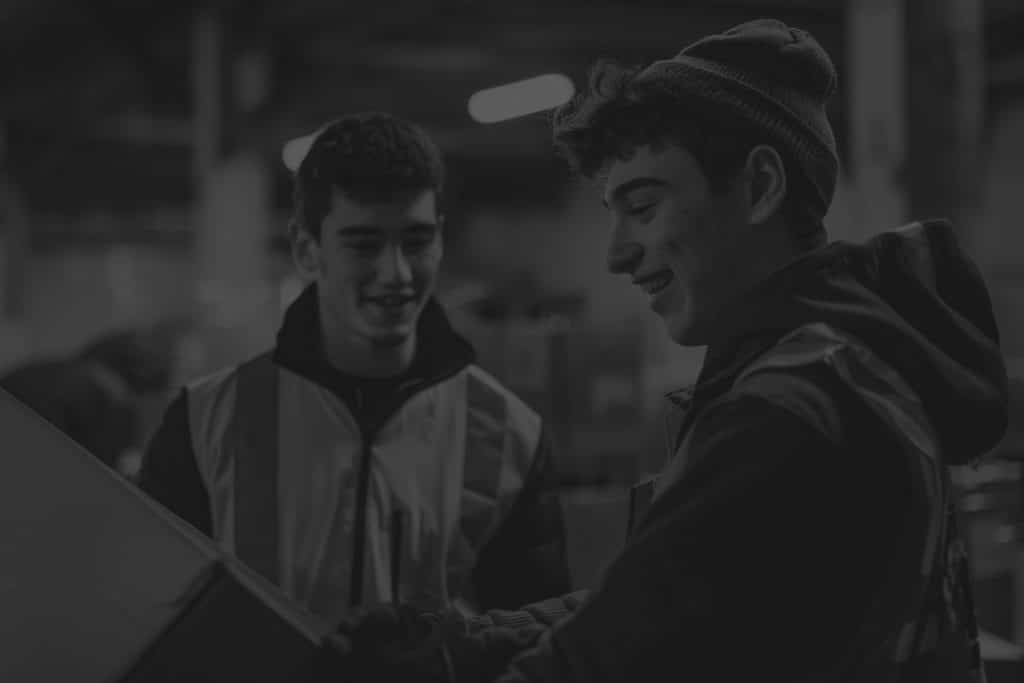 two young male workers in warehouse smiling holding box in black and white