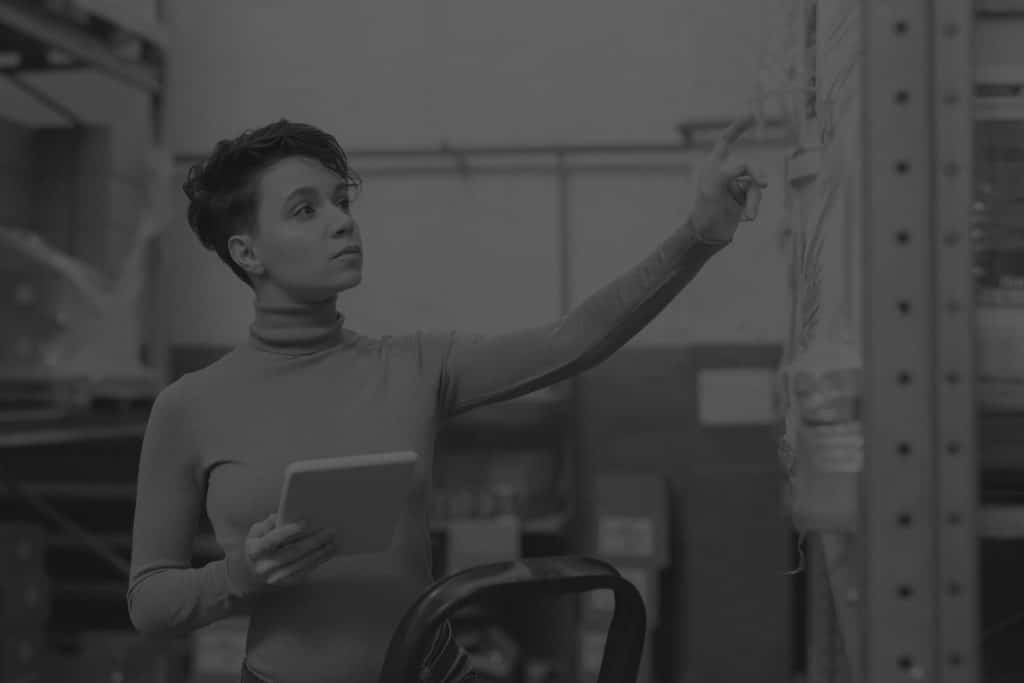 young femal logistics manager with tablet standing by rack in black and white