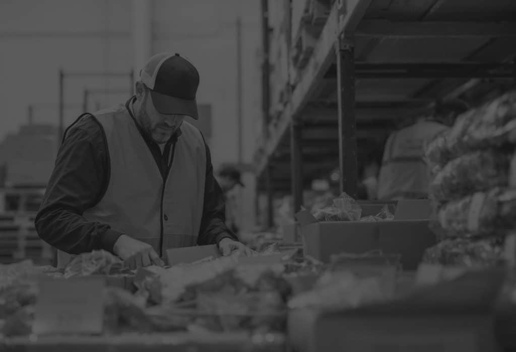 man in warehouse with hi vis picking and inspecting various food items in front of him