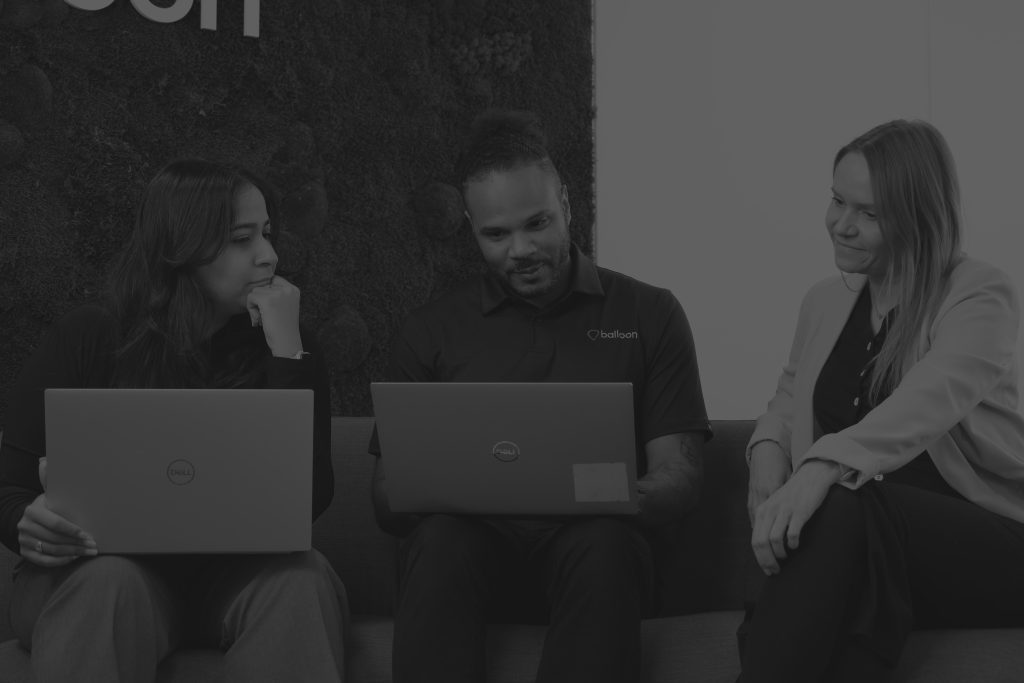 3 balloon employees smiling while working together on laptops