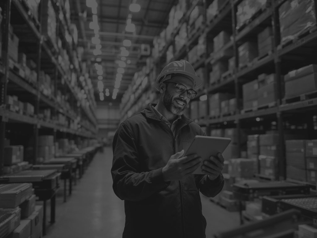 man in warehouse smiling looking at ipad black and white