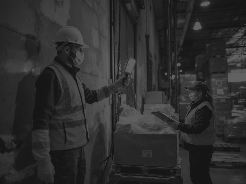 Warehouse worker shining light on box while third party auditor checks the produce