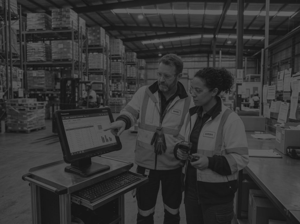 Man and woman wearing hi-vis jackets in a warehouse looking at a warehouse management system.