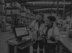 Man and woman wearing hi-vis jackets in a warehouse looking at a warehouse management system.